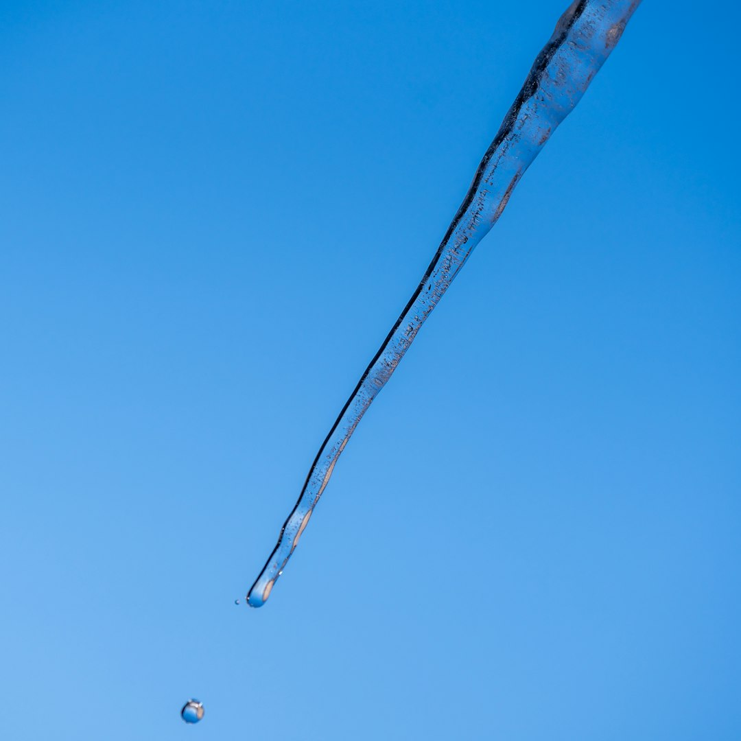 A single icicle dripping water against blue sky