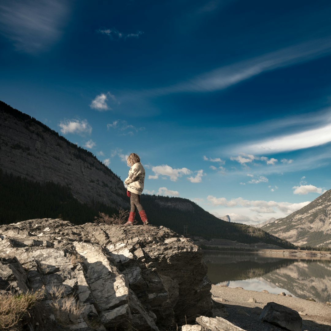Person on rocky cliff overlooking lake and mountains