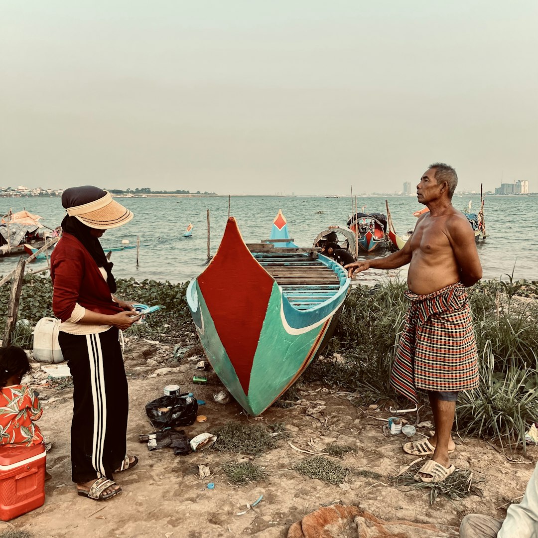 Two people stand by a colorful boat near the ocean