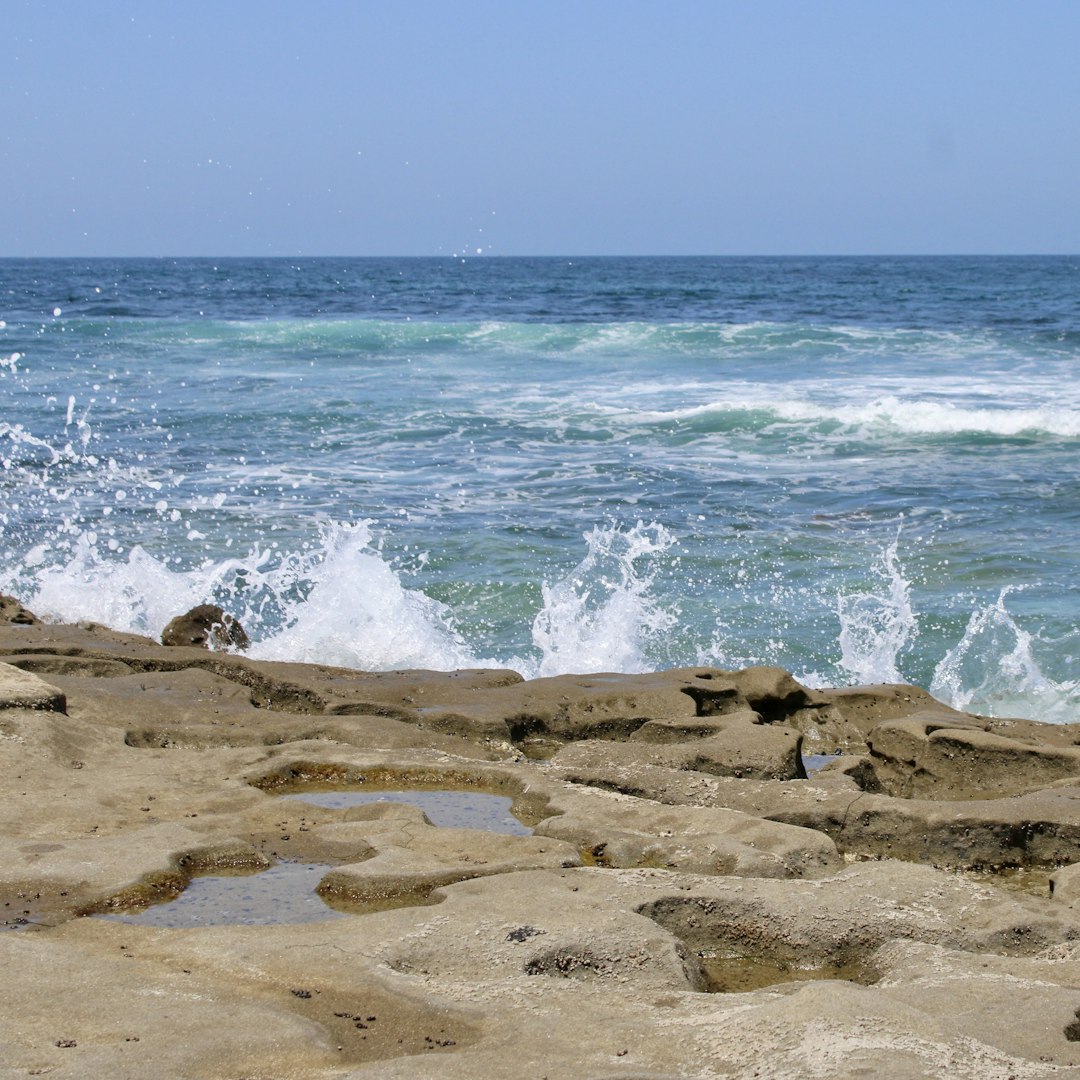 Ocean waves crash against rocky shore under a blue sky