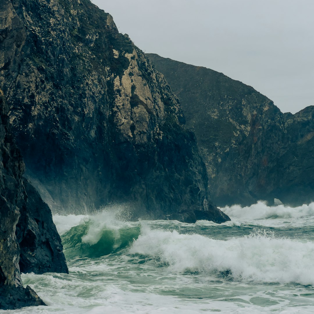 Crashing ocean waves against rocky cliffs under a cloudy sky
